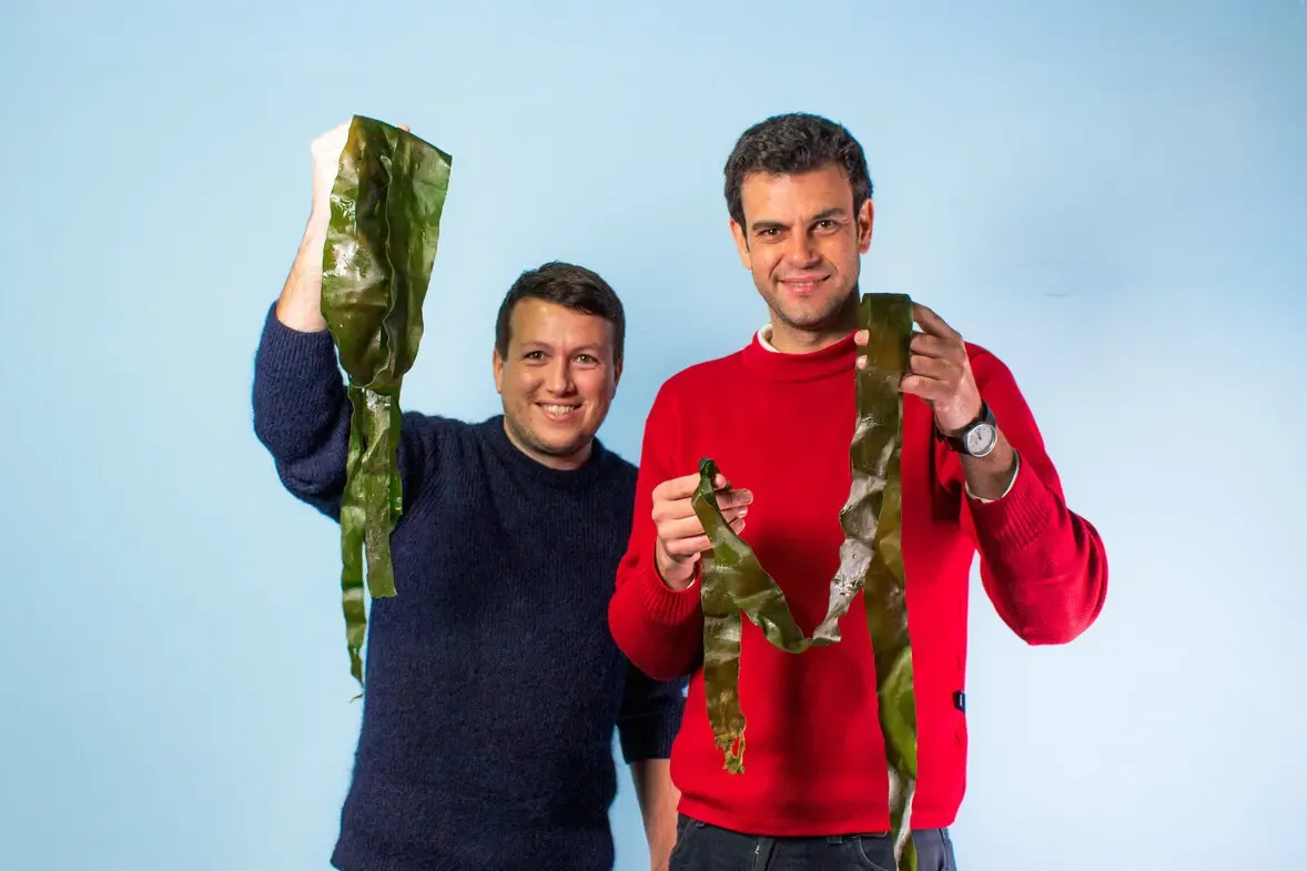 Paslier alongside co-founder Rodrigo García González, each holding seaweed—emphasizing their hands‑on role in developing Notpla’s seaweed films
