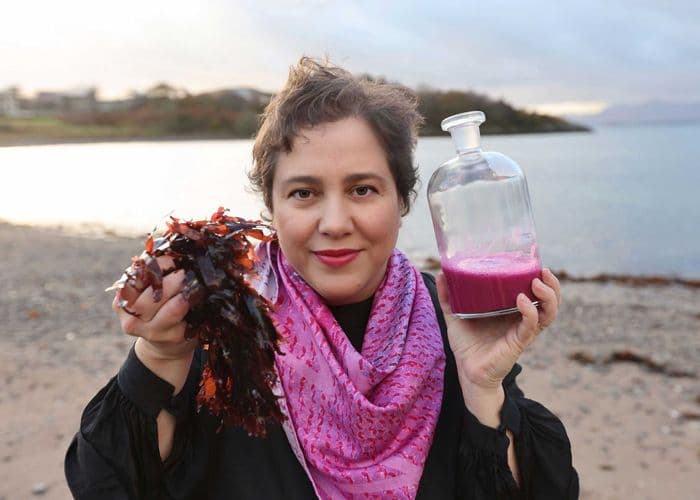 Jessica Giannotti- holding freshly harvested seaweed and a magenta pigment solution—demonstrating the raw materials and vibrant dye product